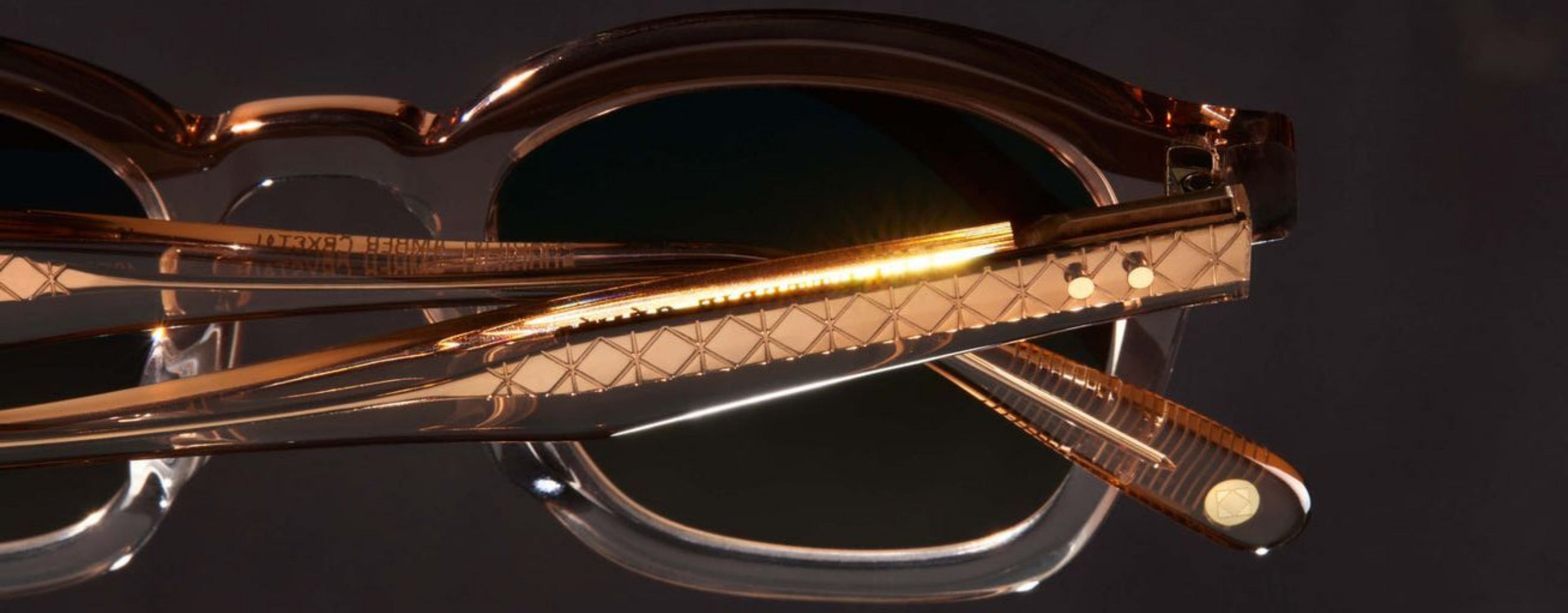 Gold-framed sunglasses with a reflective surface on a dark background