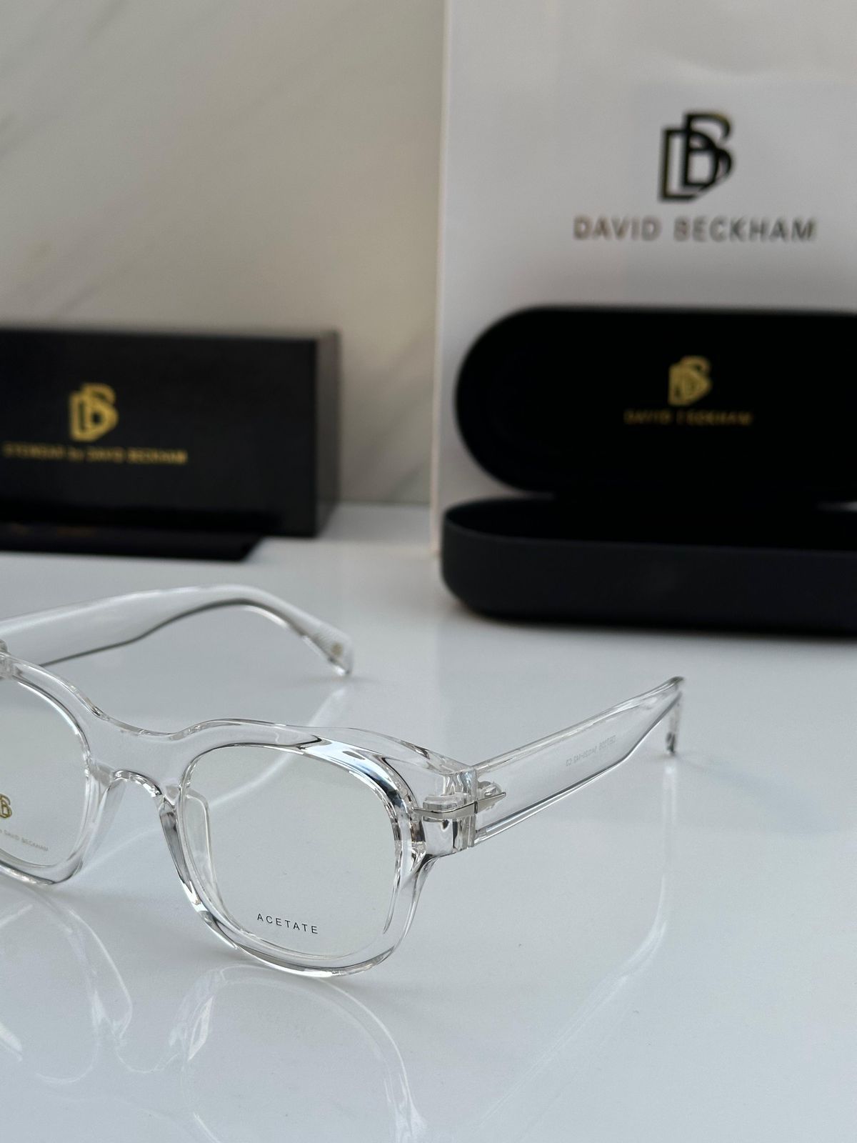 Clear eyeglasses with David Beckham branded case and packaging in the background.