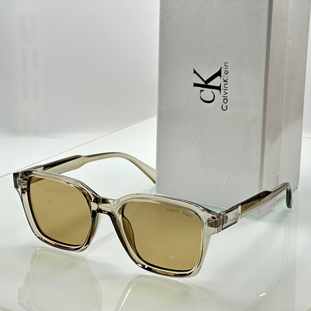 Sunglasses with brown lenses and clear frame next to a Calvin Klein box on a white background